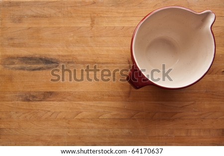 A read ceramic bowl with white interior sits on a butcher block counter with area suitable for text