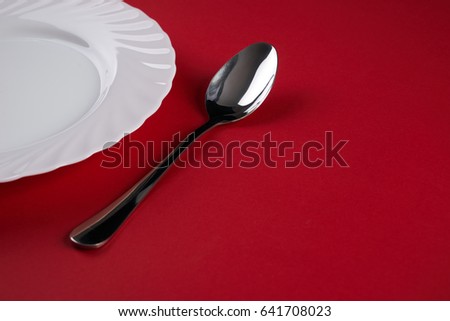 Empty white dinner plate with silver fork and Dessert Tablespoon  isolated on red tablecloth background with copy space. Table Setting. Dinner place setting