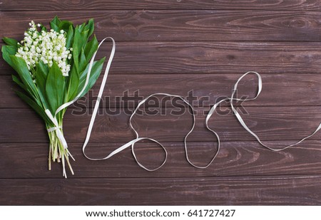 Lily-of-the-valley bouquet and love word made of the ribbon on wooden table