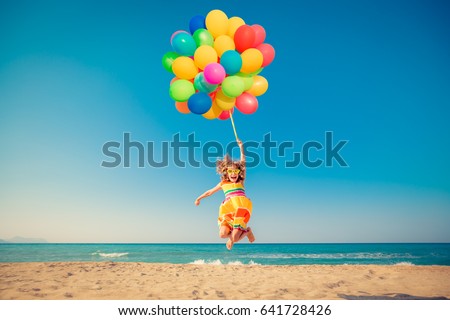 Happy child jumping with colorful balloons on sandy beach. Portrait of funny girl against blue sea and sky background. Active kid having fun on summer vacation. Freedom and imagination concept Royalty-Free Stock Photo #641728426