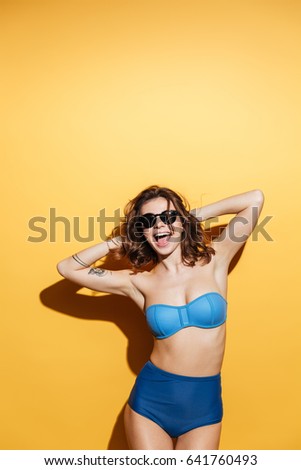 Picture of happy young woman in swimwear isolated over yellow background. Looking at camera.