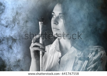 Portrait of a young adult female artist black background with a brush