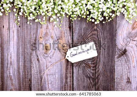 Paper tag on a rope with an inscription good morning on a gray wooden background, decorated with flowers of lilies of the valley, empty space on the left