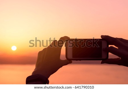 Silhouette man holding smart phone taking photo on tropical sunset beach background. Copy space travel vacation and business technology concept.