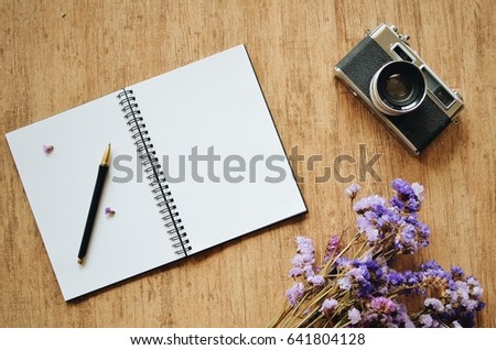 Top view of blank space notebook paper and vintage camera on wooden texture with flower 