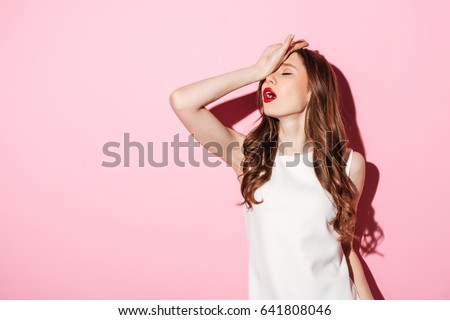 Portrait of annoyed beautiful woman placing back hand on forehead as if to say oh the tragedy of it all isolated over pink background Royalty-Free Stock Photo #641808046