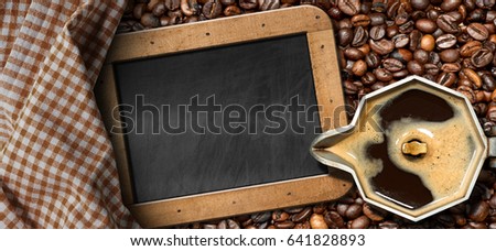 Old italian coffee maker (moka pot - top view) with roasted coffee beans on the background and an empty blackboard with copy space