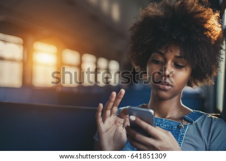 Thoughtful young biracial girl using smart phone while sitting alone in suburban train, curly african teenage female having online chat with her sister in train with copy space for your text or logo Royalty-Free Stock Photo #641851309