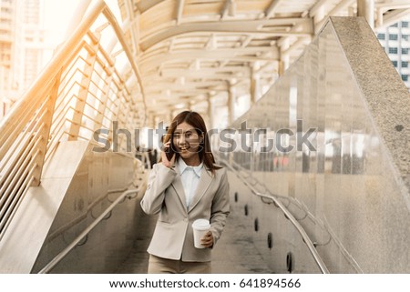 Portrait of Asian Businesswoman talking on smartphone, holding on cup of coffee and walking by the way of modern office. Business and People Concept.