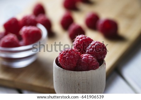Fresh and slightly imperfect raspberries in small wooden bowl, more berries in background.