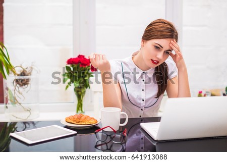Portrait of young office worker who sits at the table at the office, looks at laptop and thinks