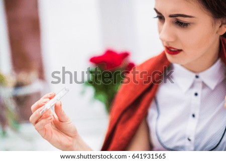 Close-up photo of sick woman who keeps thermometer in hand and looks at it indoor