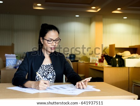 business woman look at smart phone on the left hand and right hand holding pen to write on paper, right copy space