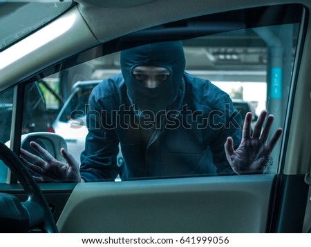 Man dressed in black with a balaclava on his head looking through car window and wondering how to break into this car. Car thief, car theft concept Royalty-Free Stock Photo #641999056