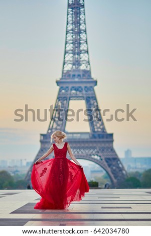 Beautiful young woman in long red dress dancing near the Eiffel tower in Paris, France