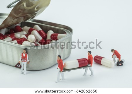 Models mini nurses transport a capsule in stretcher to the hospital, along with a canister full of white and red capsules, parody done in study of concept medicine