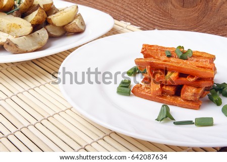 Baked carrots and potatoes with green onions on a white plate. Organic Vegetarian Food on a bamboo mat