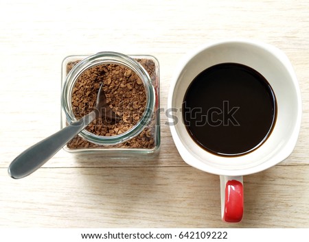 soluble instant coffee powder with silver teaspoon in transparent glass jar and brewed black coffee in white ceramic cup with red handle on wood table floor in cafe, flat lay close-up top view Royalty-Free Stock Photo #642109222