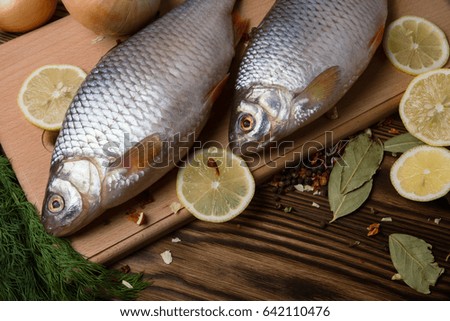 Fresh river fish on a cutting board with vegetables and spices, on a dark wooden table