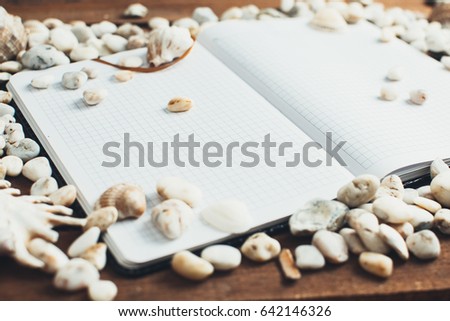 Travel and leisure, on a wooden table is a notebook next to scattered seashells