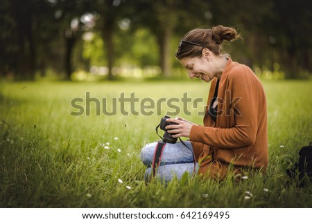 Young woman, a professional photographer, reviewing and checking images she has taken while sitting in the beautiful green grass