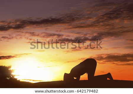 Silhouette asian muslim man with cap praying to god over sunset background