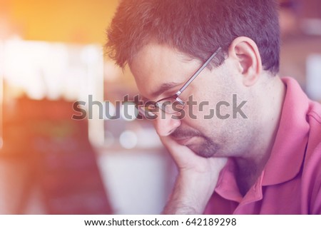 a man wearing eye glasses thinking and sitting in coffee shop, filtered tones