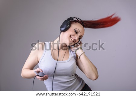 Young funky modern dancer dancing to the rhythm of the music she's listening on her phone, happy and cheerful, red fiery hair tied in a pony tail