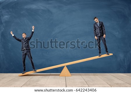 Two businessmen standing on a wooden seesaw, one happy and one sad looking. Success and failure. Business and workplace competition. Losers and winners. Royalty-Free Stock Photo #642243406
