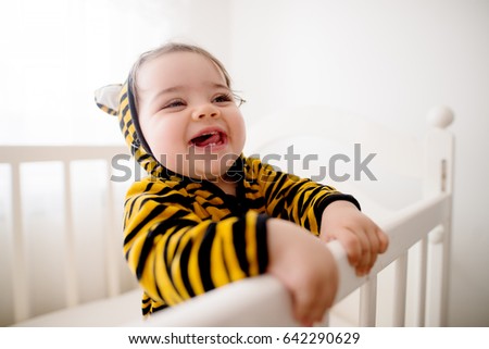 Cute baby wearing a tiny tiger costume. Having fun in her crib. Royalty-Free Stock Photo #642290629