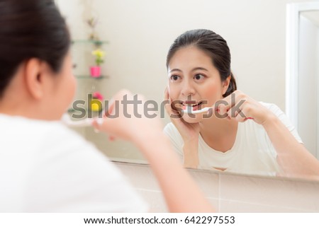 smiling beauty woman looking mirror reflection image brushing teeth and check face skin standing on bathroom in morning at home.
