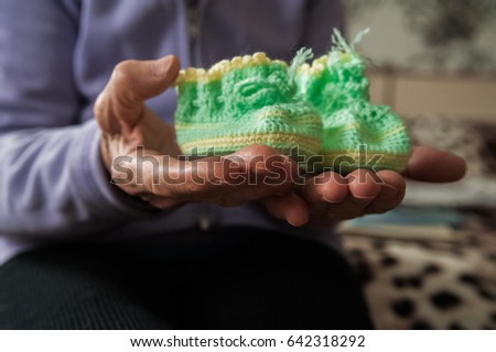 Booties in the hands of an elderly woman. Baby green booties in the wrinkled hands of an elderly man