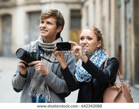 Two smiling young travellers making photo with digital camera and mobile phone