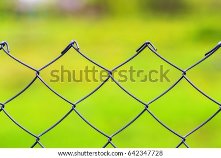 Closeup image of mesh wire fence at green grass outdoors background.