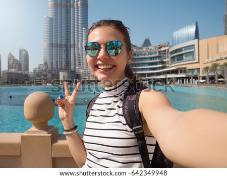 Pretty young woman tourist takes selfie portrait at Dubai fountain,Burj Khalifa. Beautiful female student takes photo for travel blog.