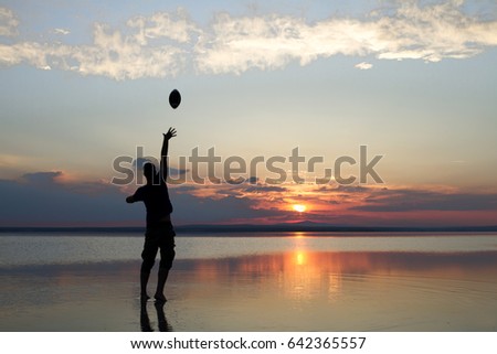 Silhouette of a boy playing american football or rugby at the beach with beautiful sunset background Childhood, serenity, sport, lifestyle concept.