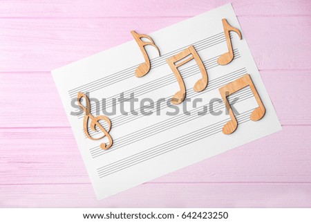 Musical notes lying on music sheets on pink wooden background