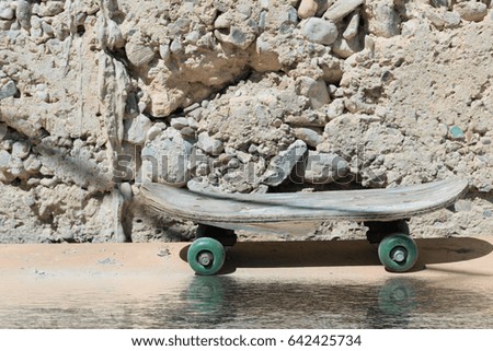 Summer: old skateboard on the background of the stone wall- reflected in water.