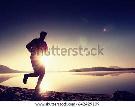 Running man on beach. Sportsman run in baseball cap, jogging guy during the sunrise above sandy beach. Man jumping on the beach at sunset