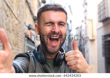 Handsome man taking a selfie and giving a thumbs up and a wink outdoors