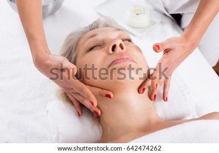 Aged smiling woman having professional face massage in spa salon 