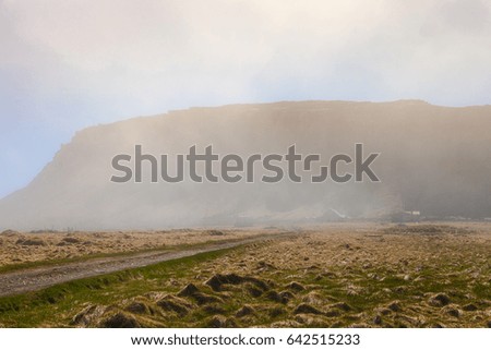 The road from gravel and several small houses in a fog on the shore of the fjord in the east of Iceland