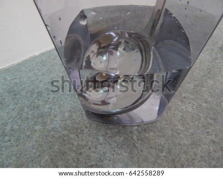 Water refraction and reflections of a soup ladle immersed in water in a clear glass container standing on a gray marble worktop. 