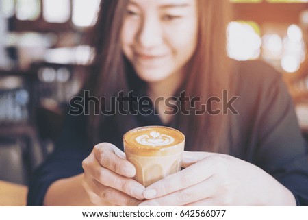 Closeup image of a beautiful Asian woman holding and showing hot coffee in vintage cafe