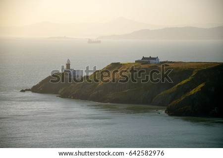Irish landscape with lighthouse, cliffs and dramatic sunset sky. 