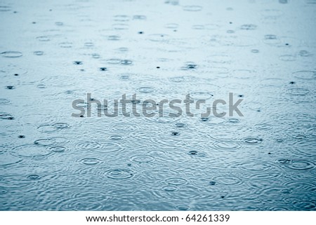 Rain drops rippling in a puddle with blue sky reflection Royalty-Free Stock Photo #64261339