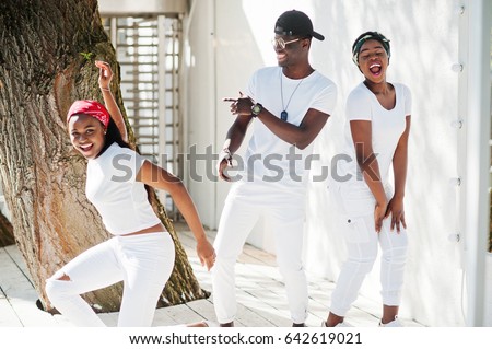 Three stylish african american friends, wear on white clothes. Street fashion of young black people. Black man with two african girls dancing gangsta rap style.