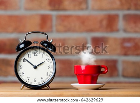 photo of cup of hot fresh coffee and alarm clock on the wonderful brick wall background