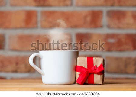 photo of cup of hot fresh coffee and gift on the wonderful brick wall background