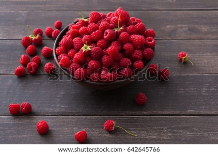 Raspberries bowl on rustic wood background. Organic berries with peduncles and green leaves on wooden table
